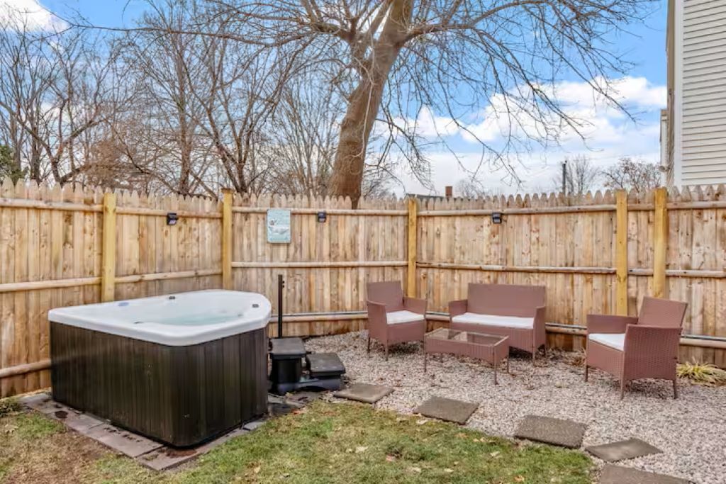A backyard with a hot tub, wicker furniture, and a wooden fence.