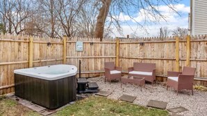 Patio trasero con jacuzzi, mobiliario de mimbre y valla de madera.