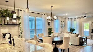 Una cocina amplia con encimera de granito, un comedor con una mesa redonda y sillas, y una sala de estar con sofá y ventilador de techo.
