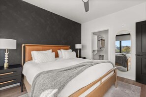 Une chambre à coucher moderne avec un grand lit, des lampes de chevet, un miroir et une vue sur l’extérieur, visible à travers une porte ouverte.