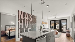A modern kitchen with a central island, a dining area with a view, and a bedroom with a cityscape wall.