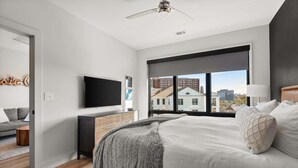 A bedroom with a large window, a bed, a TV, and a ceiling fan.