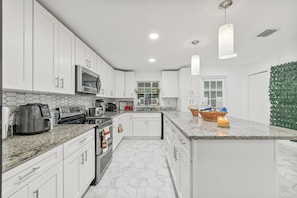 A modern kitchen with white cabinets, a microwave, a stove, and a granite countertop.