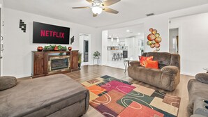 Ein modernes Wohnzimmer mit Kamin, Deckenventilator und einem Flachbildfernseher, der 'NETFLIX' anzeigt.