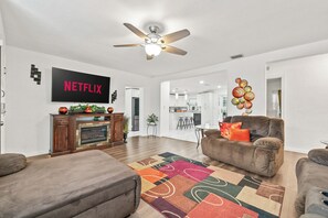 Un soggiorno moderno con camino, ventilatore a soffitto e televisione a schermo piatto che mostra 'NETFLIX'.