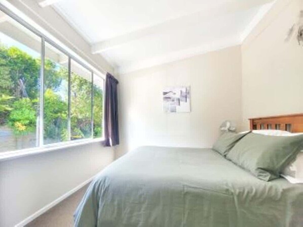 Ein Schlafzimmer mit großem Fenster, einem Bett und einer Wandleuchte.