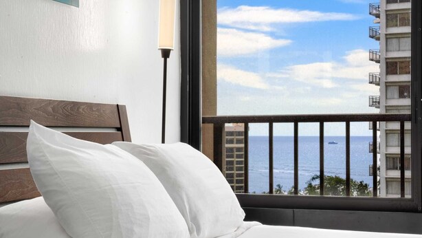 Ein Hotelzimmer mit Bett, weißen Kissen, Meerblick und einem Balkongeländer.