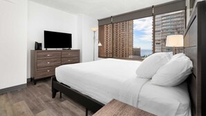 Ein modernes Hotelzimmer mit einem großen Bett, einem Flachbildfernseher auf einer Holzkommode und Blick auf hohe Gebäude.
