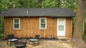 Une petite cabane en bois avec deux fenêtres, une porte et un foyer avec des chaises.