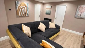 A modern living room with a sectional sofa, wooden flooring, and artwork on the walls.