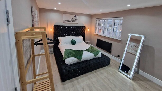 A bedroom with a bed, a wooden ladder, a wall-mounted TV, and a window with blinds.