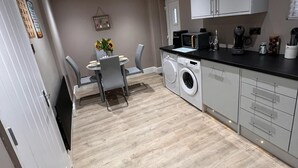 A compact kitchen with a washing machine, a dining area with a table and chairs, and a small window.