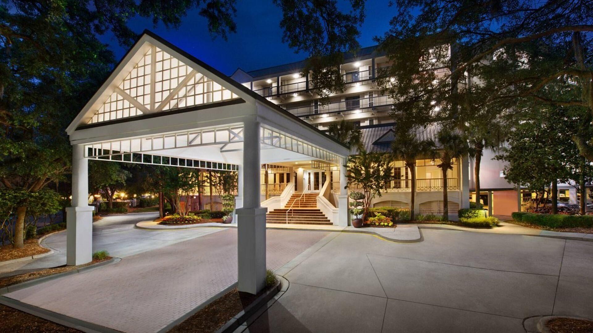 Una entrada de hotel moderna con un vestíbulo cubierto, una escalera que conduce al edificio y zonas ajardinadas.