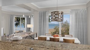 A modern dining area with a view of the sea, a large chandelier, and a dining table set for four. - Marriott’s Harbour Club 2-Bedroom Villas – The Perfect Lowcountry Getaway (Hilton Head Island)