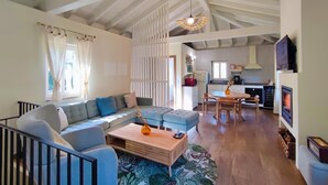 A spacious living room with a sofa, coffee table, and a fireplace. There is a kitchen area with a dining table and chairs.