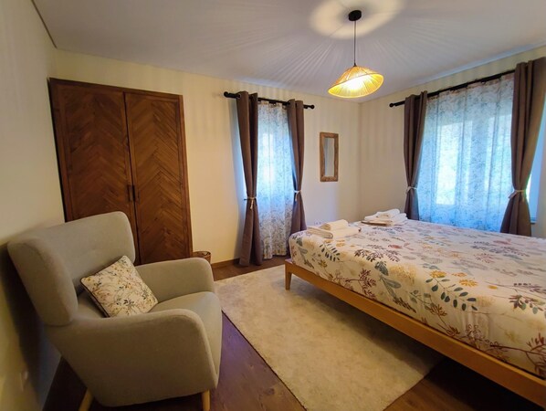 A bedroom with a bed, a chair, a wardrobe, and a hanging light fixture.