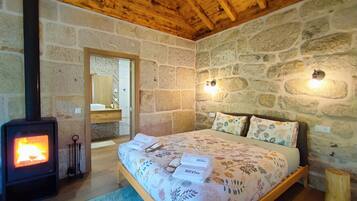 Un dormitorio con pared de piedra, techo de madera, cama con ropa de cama floral y estufa de leña.