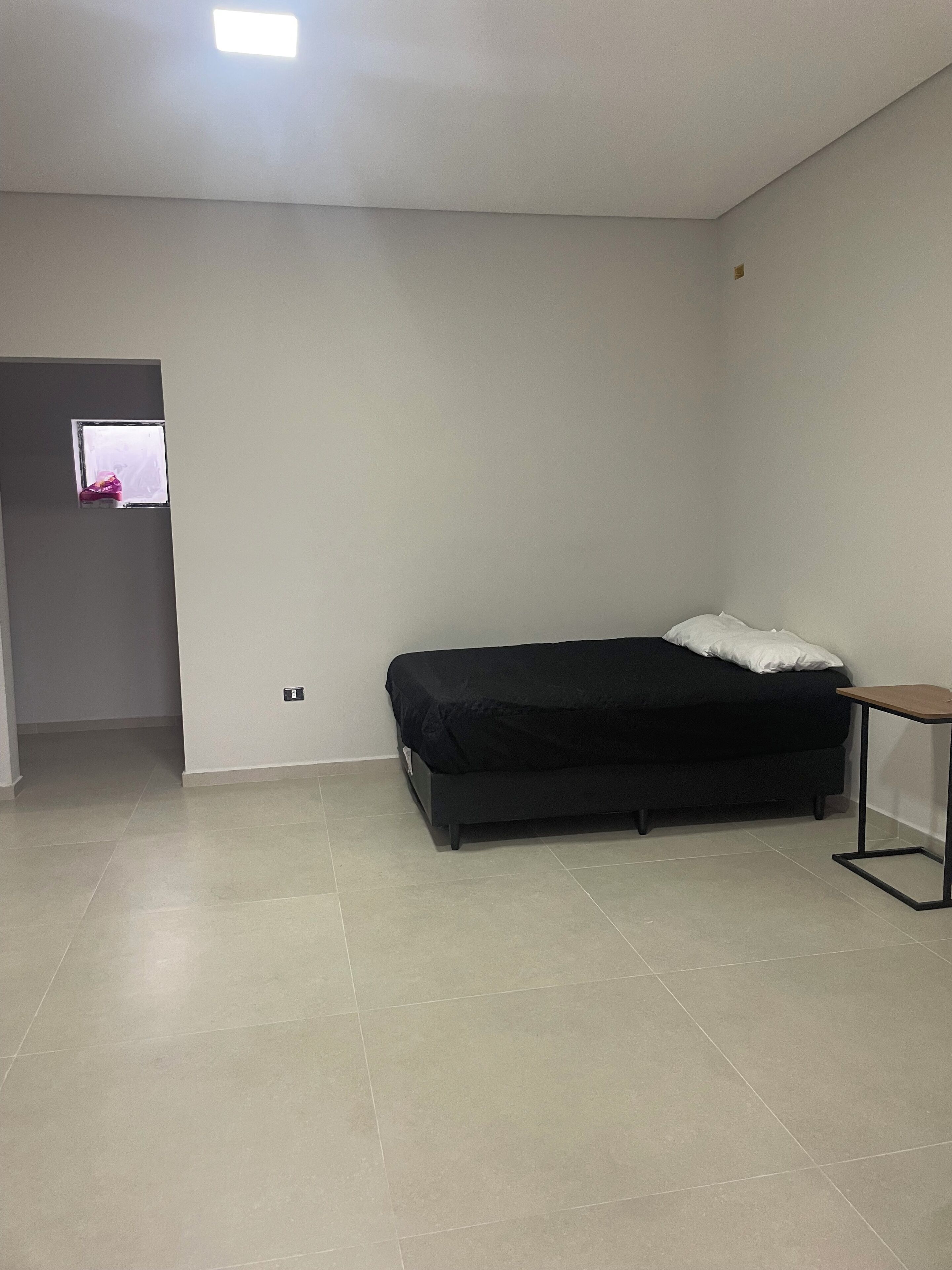 Una habitación con cama, una mesita y una puerta con ventana.