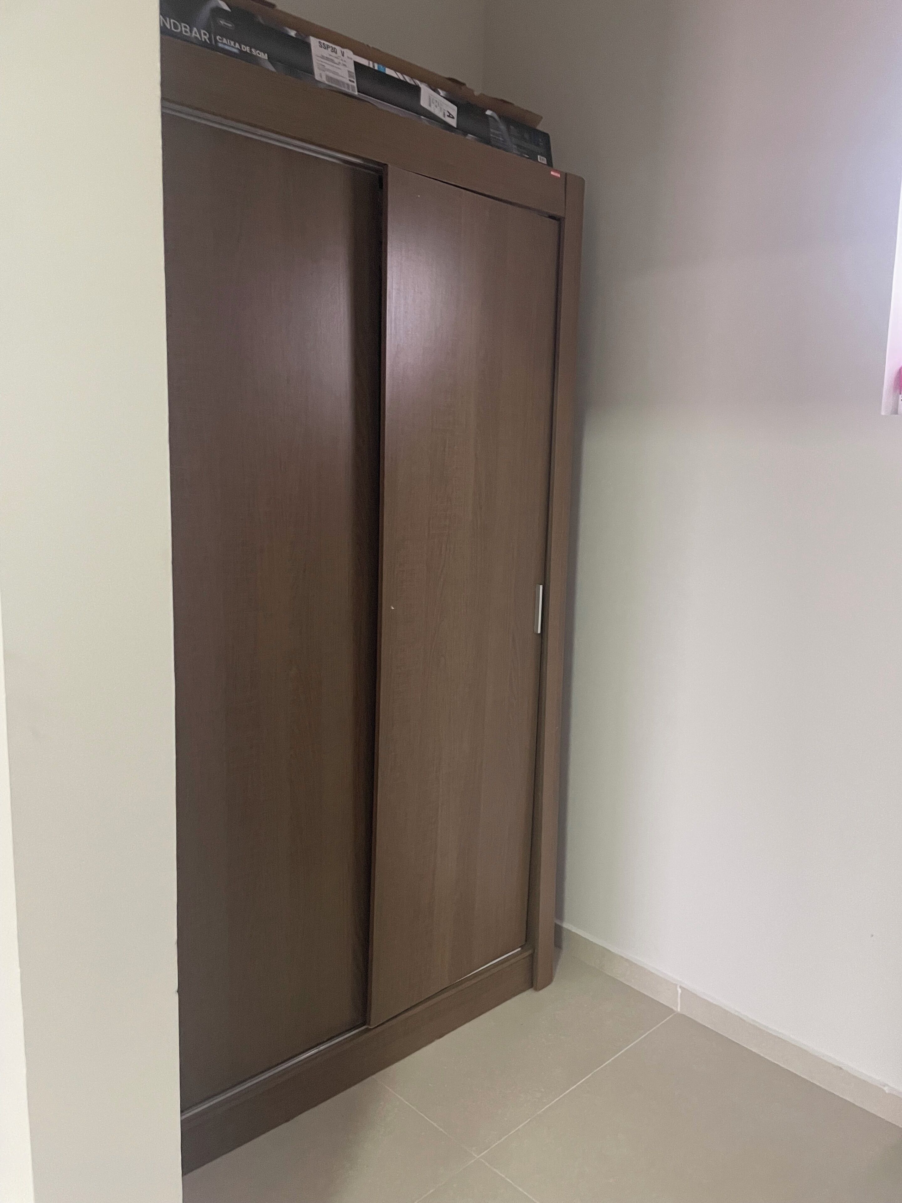 Ein geschlossener Holzschrank mit Griff, in einem Raum mit weißen Wänden und Fliesenboden.