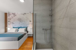 Un dormitorio moderno con cama, mesitas de noche y zona de ducha con puerta de cristal.