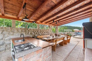 Cocina exterior con pared de piedra, mobiliario de madera y estufa a gas.