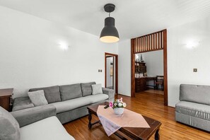A modern living room with a grey sofa, a wooden coffee table with a vase of flowers, and a black pendant light.