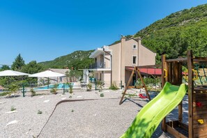 A residential area with a pool, a wooden play structure, and a house with a balcony.