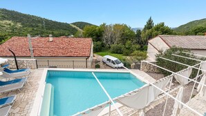 A swimming pool with a clear view of the surrounding landscape, including hills and a building with a tiled roof.