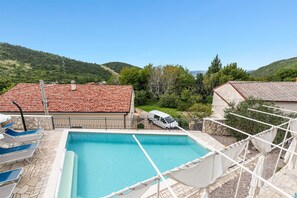 A swimming pool with a clear view of the surrounding landscape, including hills and a building with a tiled roof.