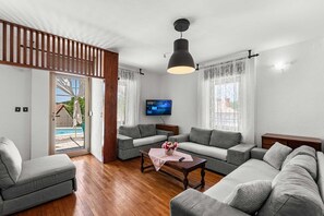 A modern living room with a grey sofa set, a wooden coffee table, and a flat-screen TV mounted on the wall.