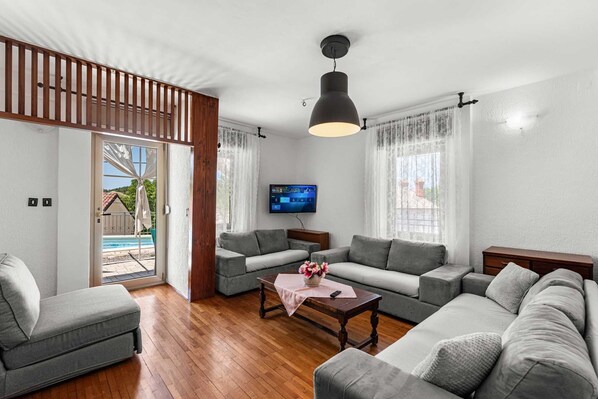 A modern living room with a grey sofa set, a wooden coffee table, and a flat-screen TV mounted on the wall.