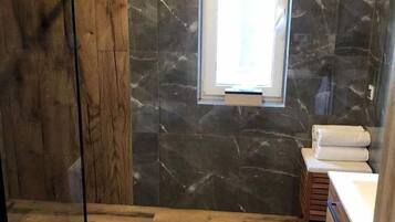 A bathroom with a wooden floor, a marble wall, a window, a toilet, and a wooden vanity with a sink.