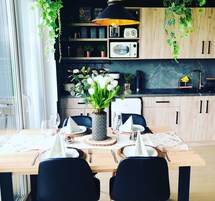 Una cocina moderna con armarios de madera, encimera negra y comedor con una mesa para dos.