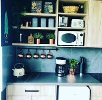 Una cocina con microondas, cafetera, hervidor y ollas colgadas.