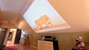 Een kamer met een projectie van een leeuw op het plafond, een bureau met een computer, een stoel en een klein tafeltje met een lamp.