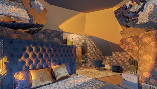 Een slaapkamer met een gestoffeerd hoofdeinde, beddengoed met bloemenprint, een blauwe fauteuil en een heater in vintage-stijl.