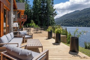 A wooden deck with outdoor furniture, a stone wall, and a view of a lake and mountains. - Puerto Manzano Boutique Hotel (Villa La Angostura)