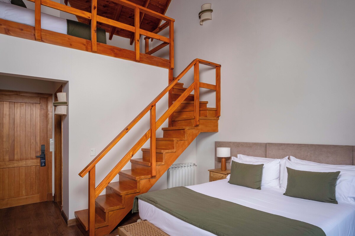 A bedroom with a wooden staircase, a bed with white and green bedding, a nightstand with a lamp, and a radiator.