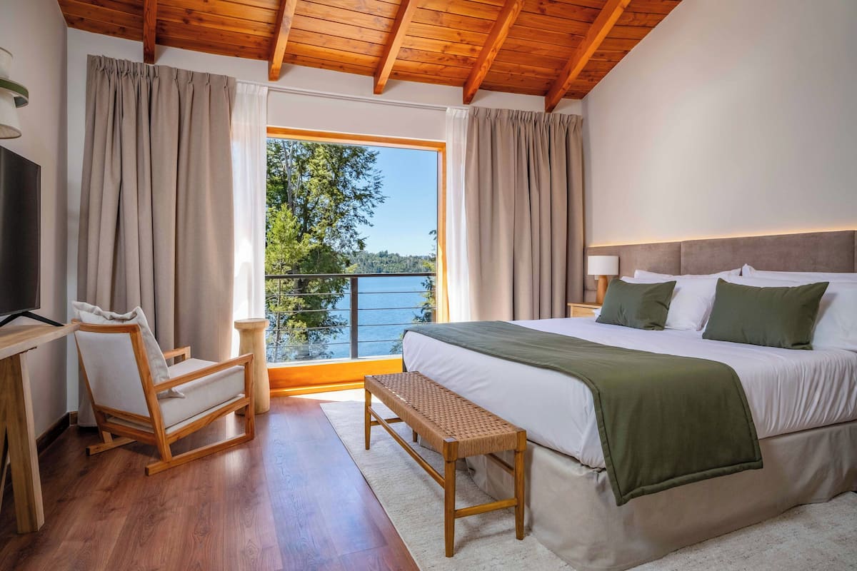 Une chambre avec un lit, un banc en bois, une télévision et une vue sur un lac.