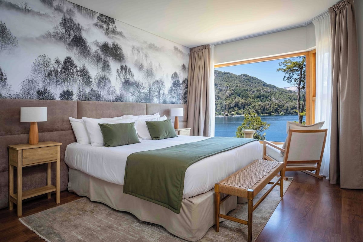 Une chambre à coucher avec un grand lit, une table de chevet, une chaise et une vue sur un lac et des montagnes.