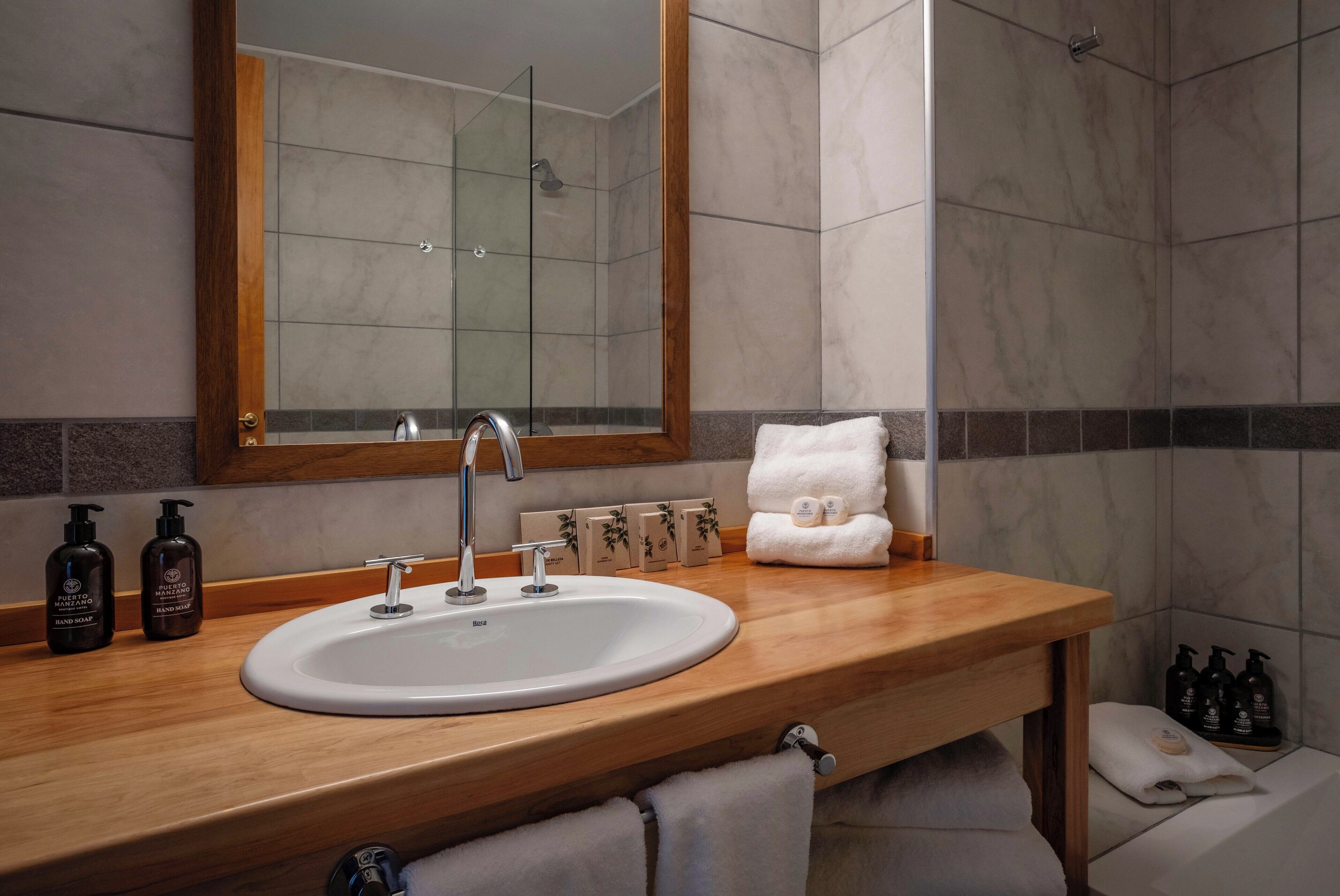Un baño con tocador de madera, lavabo blanco, espejo y zona de ducha.