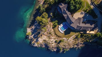 Vista aérea de una propiedad costera con piscina, un edificio curvo y una zona de estacionamiento.