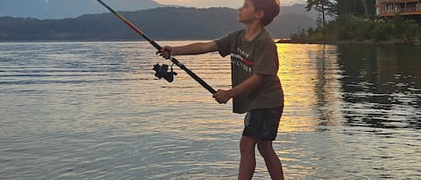 A person fishing by a lake with mountains in the background.