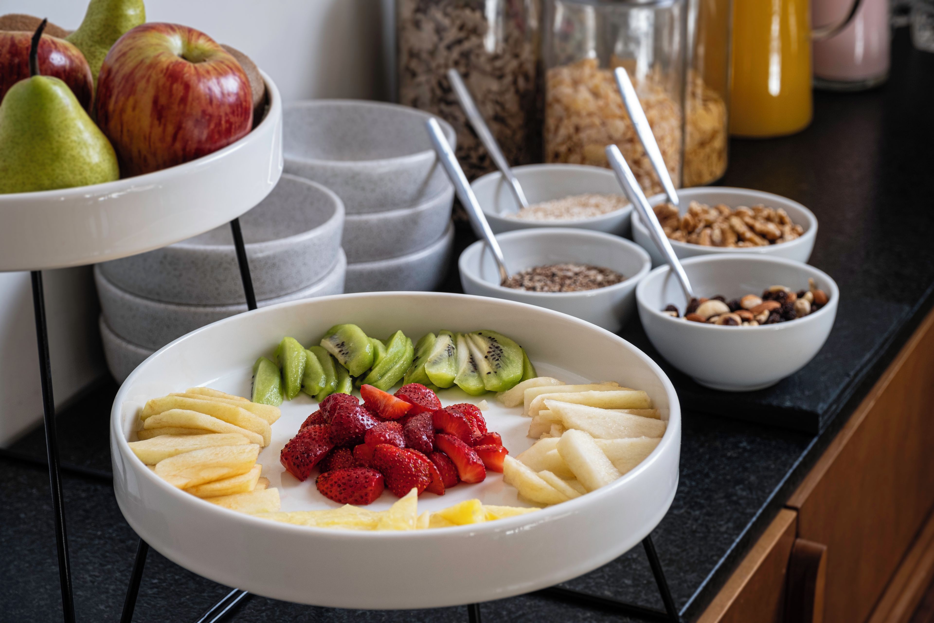 En frukostuppläggning med en skål med frukt, flingor och en burk honung.