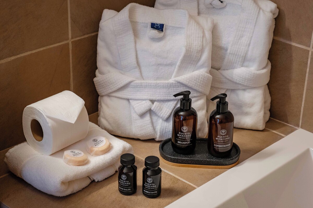A bathroom with a bathtub, a white robe, toiletries including a bottle of shampoo and conditioner, and a roll of toilet paper.