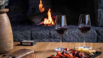 Una mesa de madera con dos copas de vino, un jarrón con flores, y una variedad de quesos y embutidos.