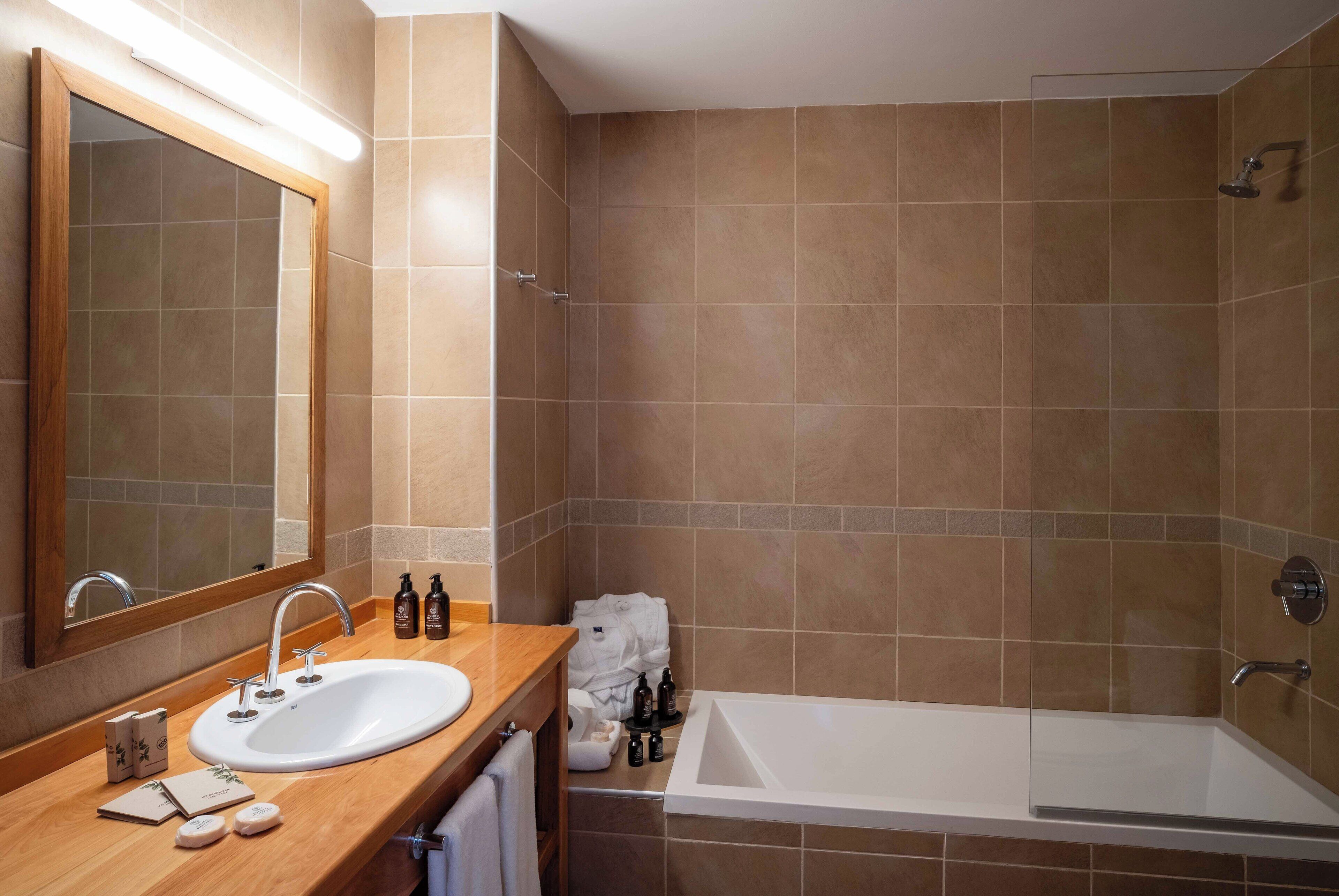 Un baño moderno con un espejo grande, un lavamanos y una bañera.