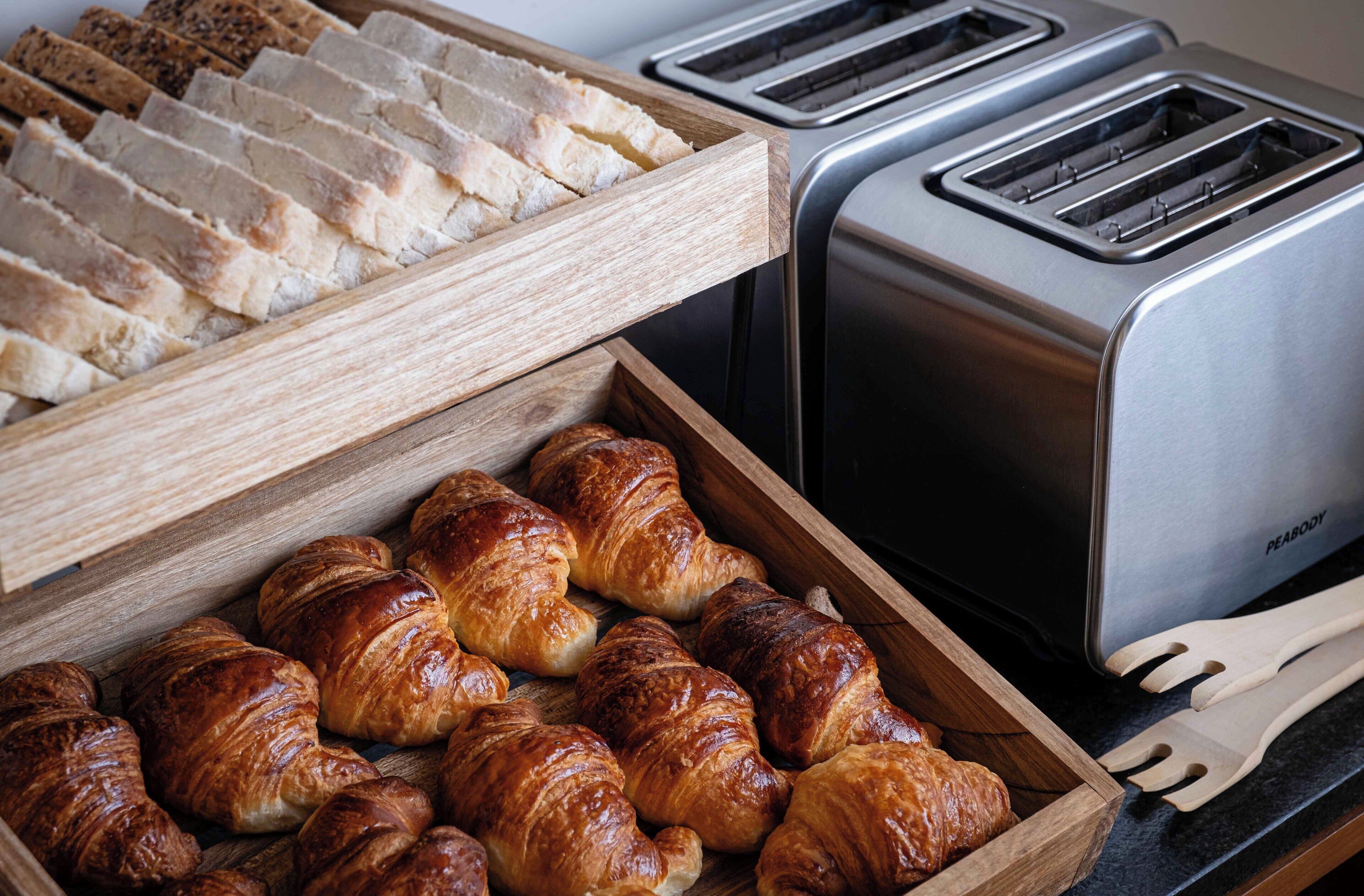 A breakfast buffet with sliced bread and croissants, and two toasters.