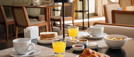 A breakfast setting with a table set for two, including plates, cups, glasses, and a croissant.