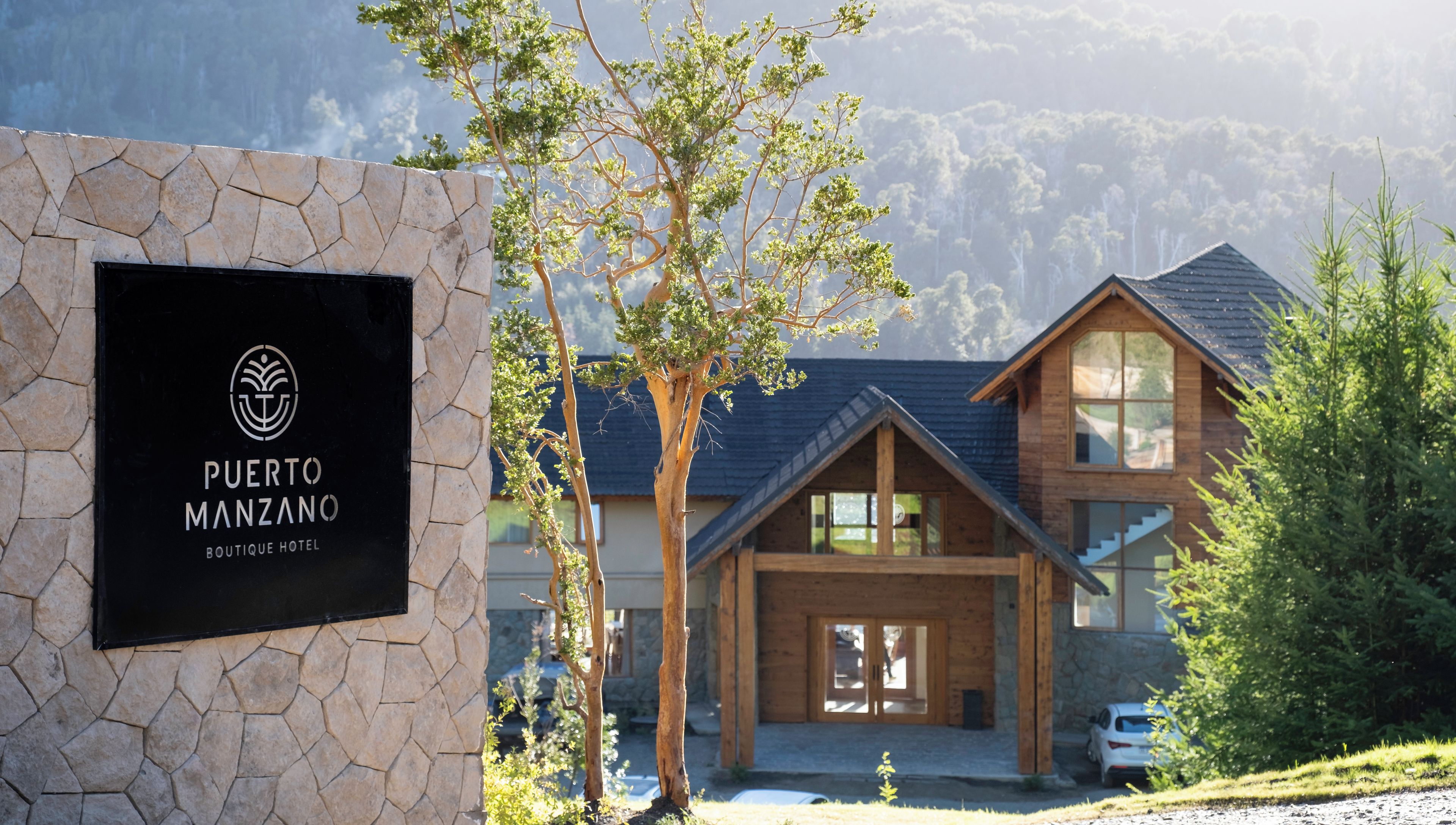 Un hôtel de charme appelé Puerto Manzano, avec une façade en pierre, un revêtement extérieur en bois et une vue sur les montagnes en arrière-plan.